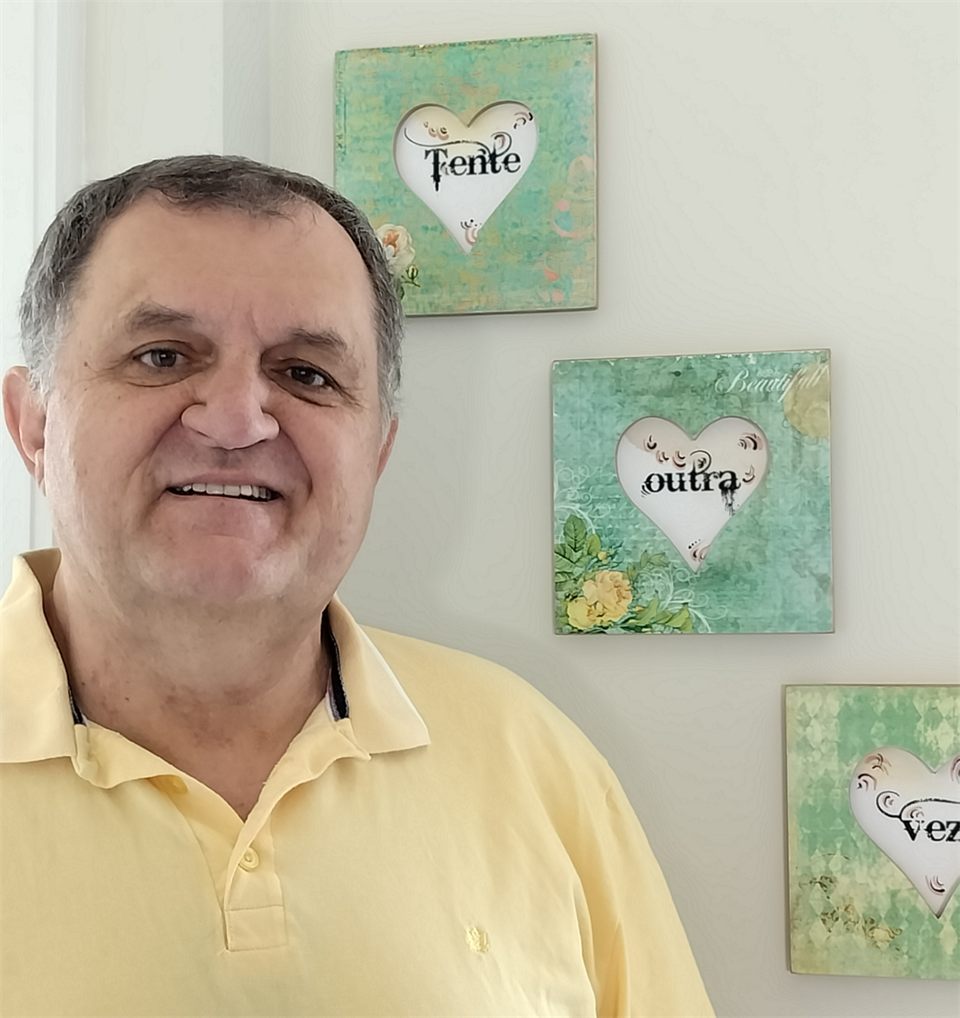 Alexandre Ari Monich sorrindo, ao lado dos quadros com a mensagem Tente outra vez