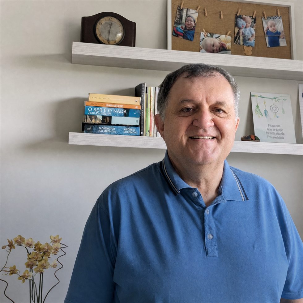 Alexandre Ari Monich, psicólogo, sorrindo, diante da estante com seus livros